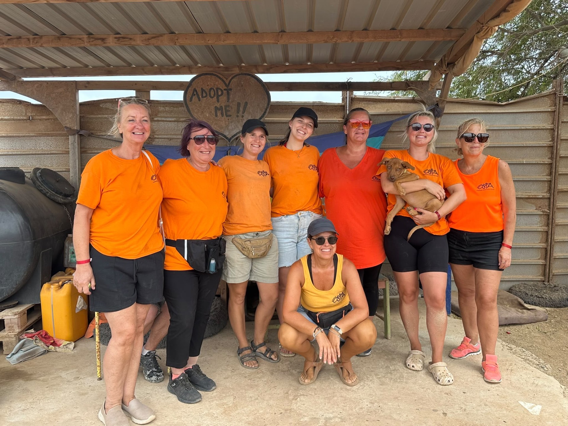 Das OSPA-Team in orangefarbenen Vereinsshirts mit einem Welpen im Tierheim auf Sal
